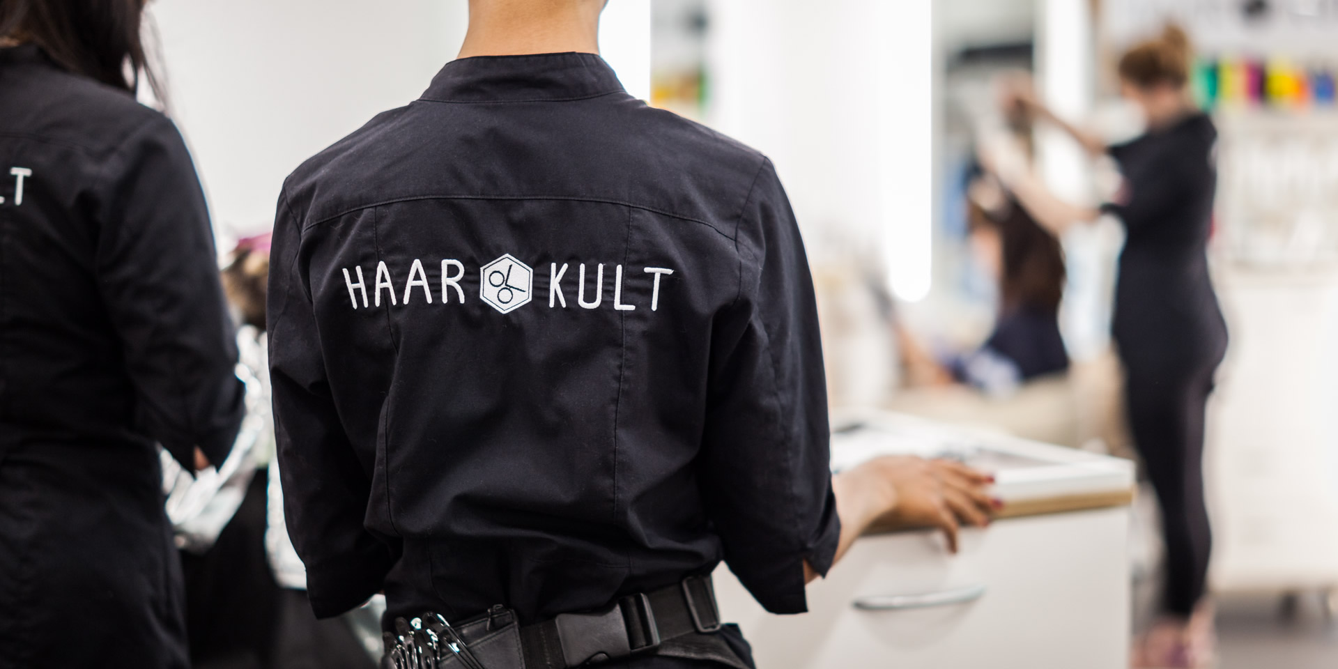 Haarkult Stylistin von hinten mit Logo auf der Jacke